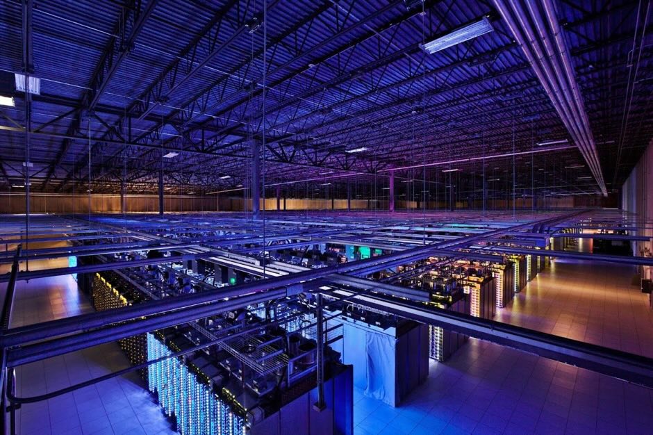 "Wide interior photograph of a Google data center aisle with rows of server racks, cable trays, and overhead lighting in Council Bluffs, Iowa."
