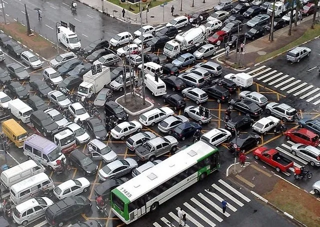 "Photograph or stylized aerial diagram of vehicles gridlocked at an intersection, each lane waiting on another in a cycle so no car can proceed—mirroring circular wait in locking. Caption ties the visual metaphor to threads holding locks while waiting on peers."